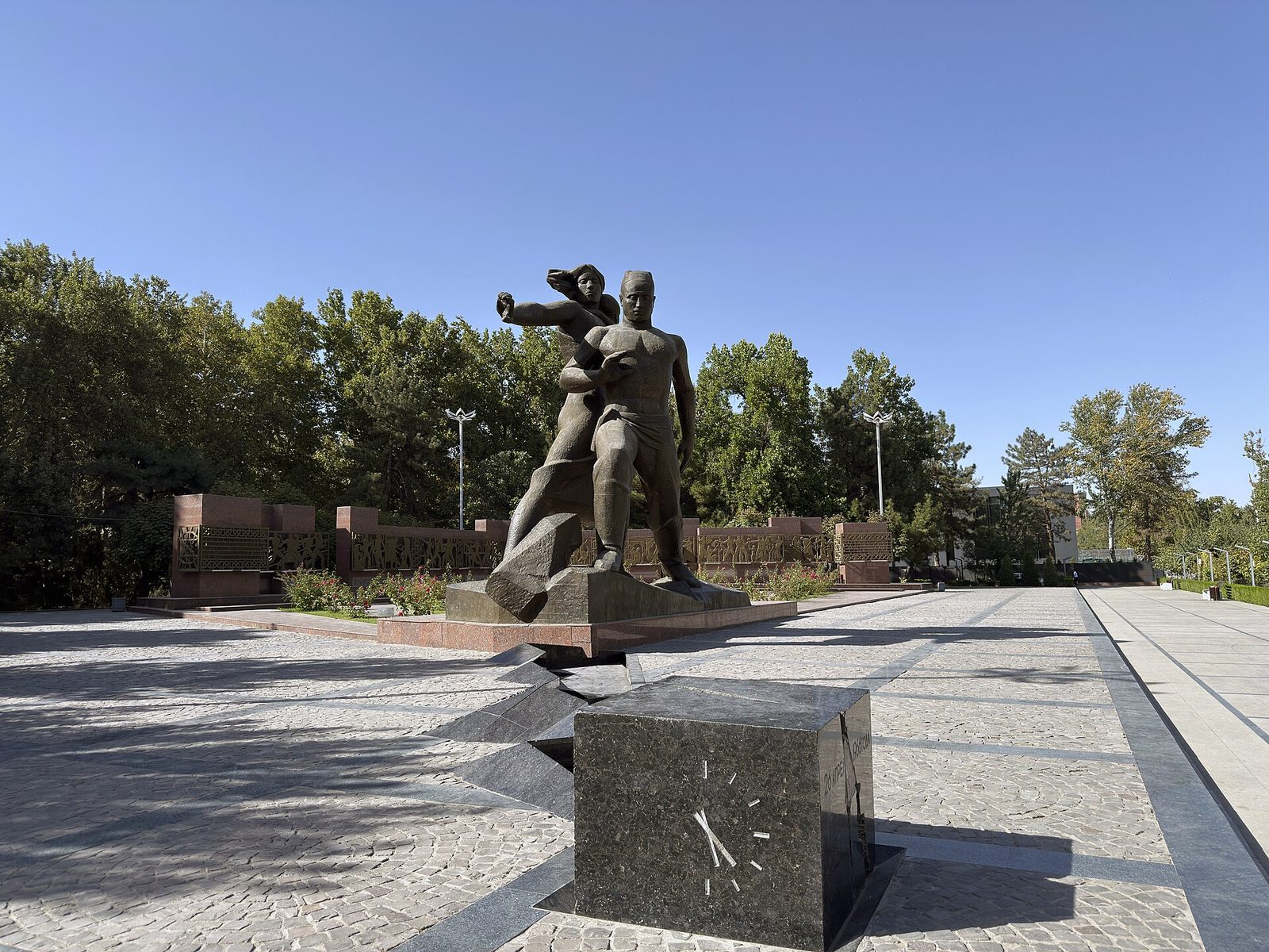 The Courage memorial: a split stone cube with a clock dial and the sculpture behind it